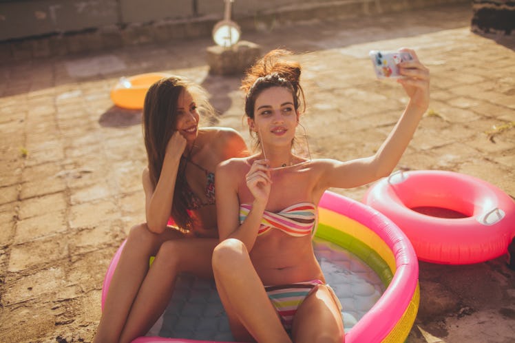 Two friends snap a selfie, while sitting in an inflatable pool.