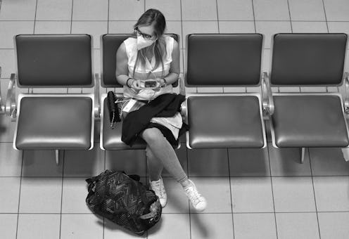 A woman with a face mask sits in a travel terminal. Self-quarantine is necessary when you travel bet...