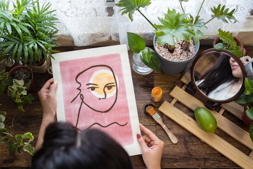 A woman holds a pink abstract painting in a windowsill garden. These seven myths about bipolar disor...