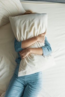 A woman with a pillow over her face. Experts explain how to get control of your stress dreams.