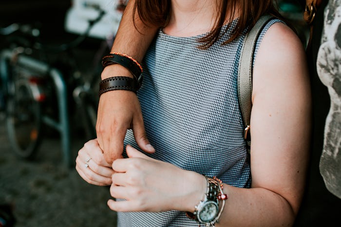 A man's hand over a shoulder of a woman wearing a grey tank top