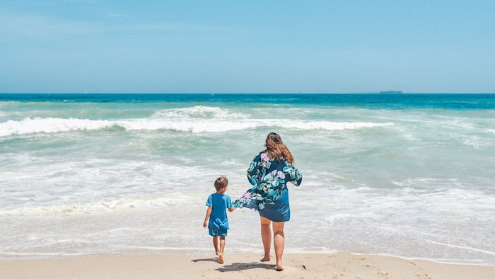 A boy holding his mother's shirt while walking toward the sea