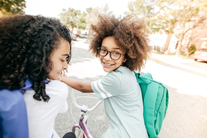 kid on bike with backpack and friend on way to school
