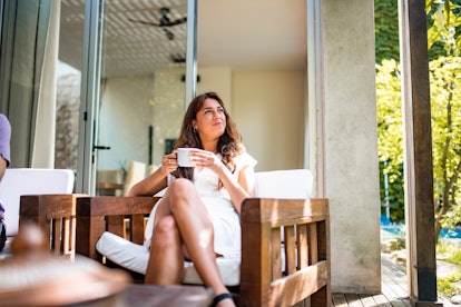A relaxed woman holds a mug in her hands, while sitting on her patio outside. 