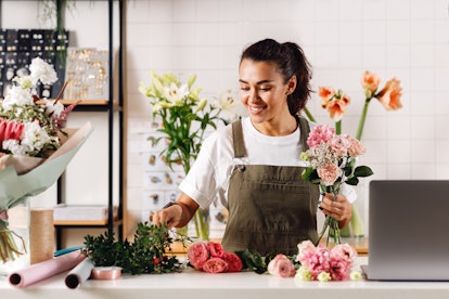 A young woman puts together a fresh flower bouquet while wearing an apron.