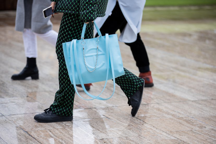 A woman wearing a black suit with green dots and a light blue Telfar shopping bag