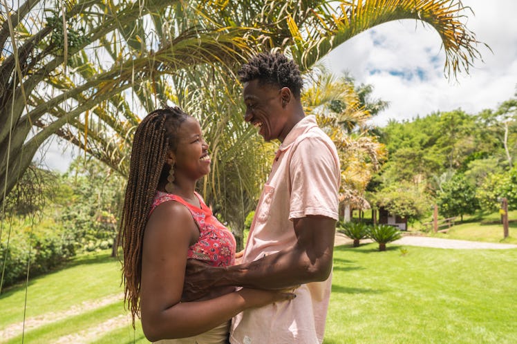 A young Black couple stands in front of a palm tree after getting engaged.