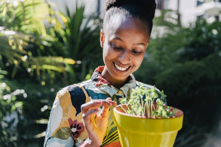 A happy woman in a floral printed button-down tends to her potted plant outside in the sunshine.