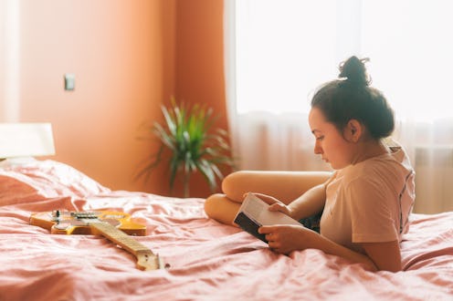 A woman with an updo reading a book while lying on a bed