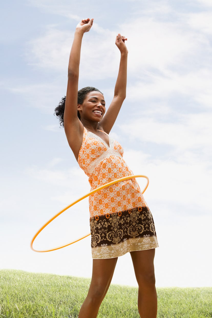 A woman hula hoops. These nostalgic outdoor activities make excellent workouts as an adult.