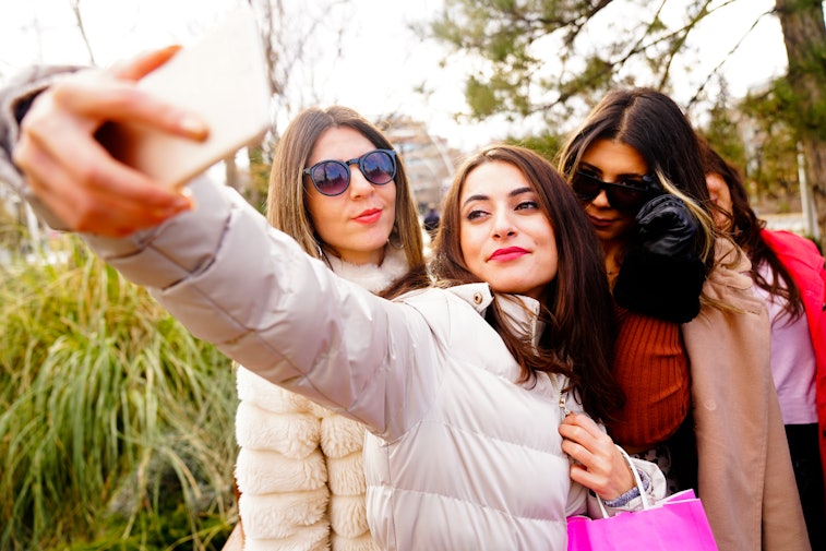 Three women posing together while one takes a selfie with her smartphone.