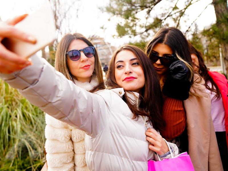 Three women posing together while one takes a selfie with her smartphone.