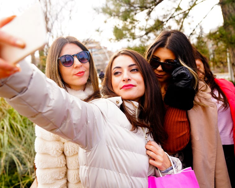 Three women posing together while one takes a selfie with her smartphone.