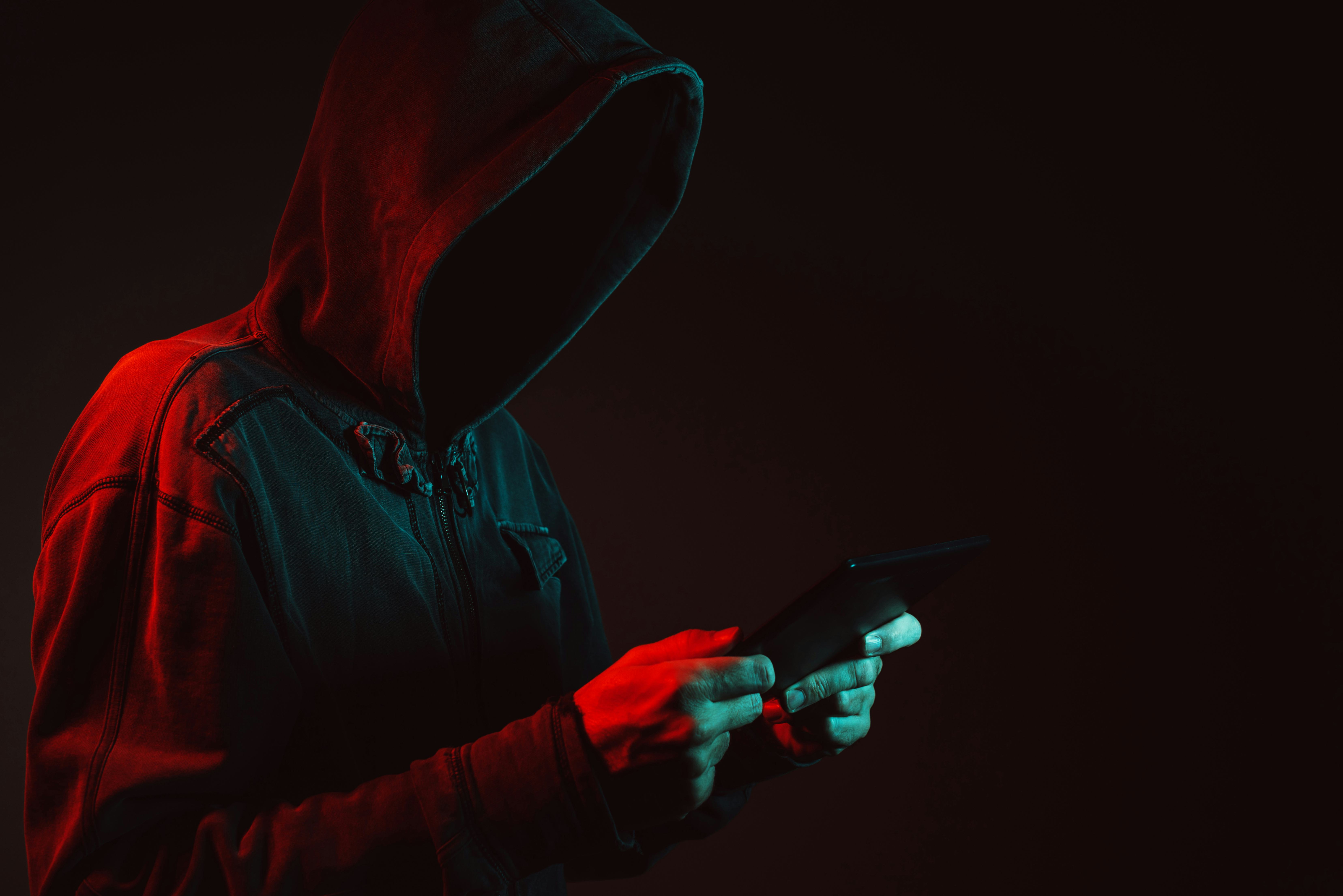 A hooded man holding a phone. Ransomware attack.