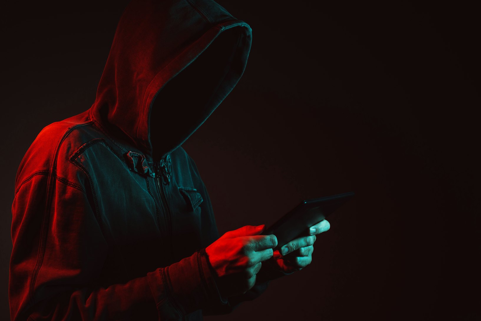 A hooded man holding a phone. Ransomware attack.
