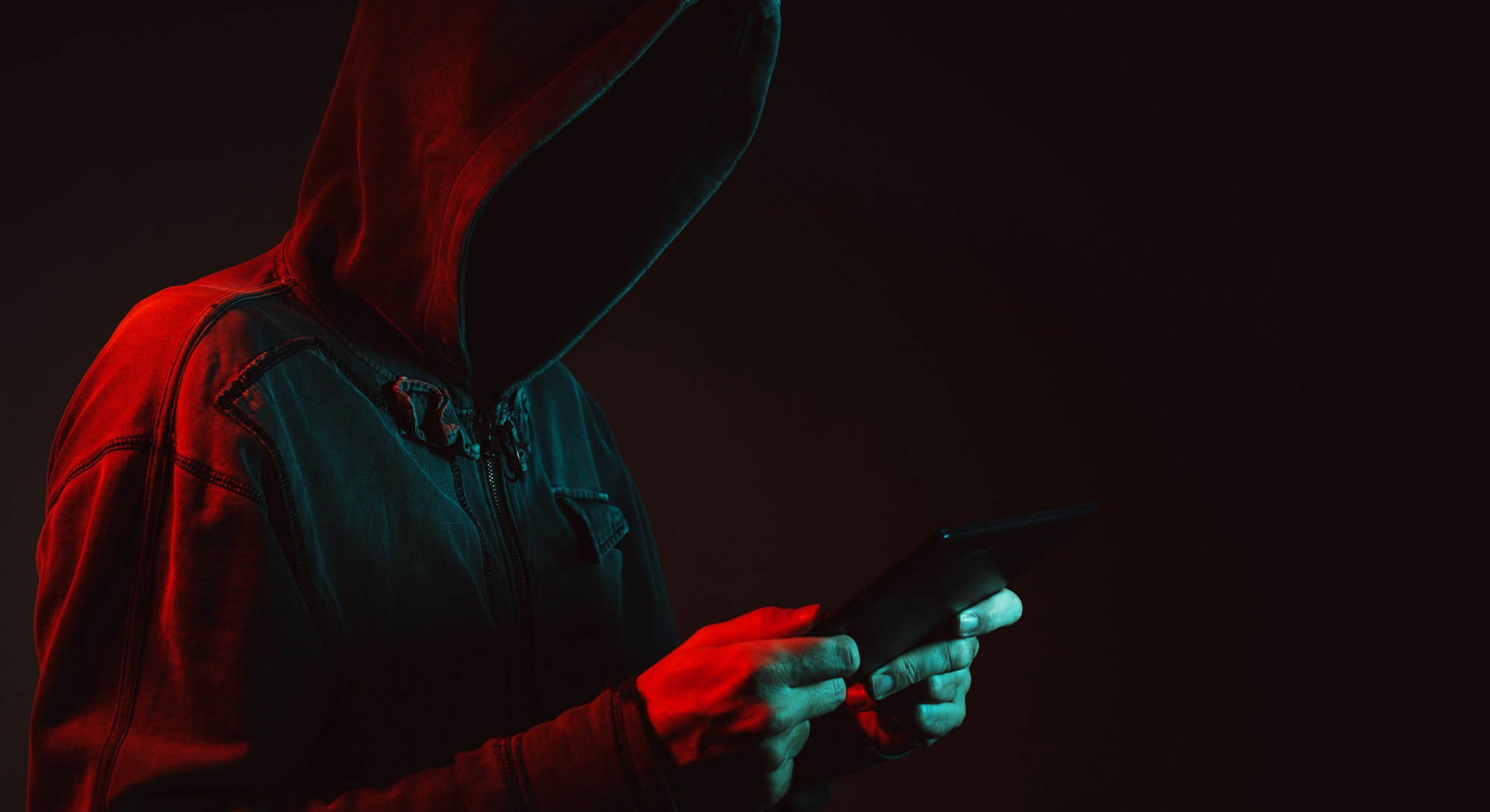 A hooded man holding a phone. Ransomware attack.