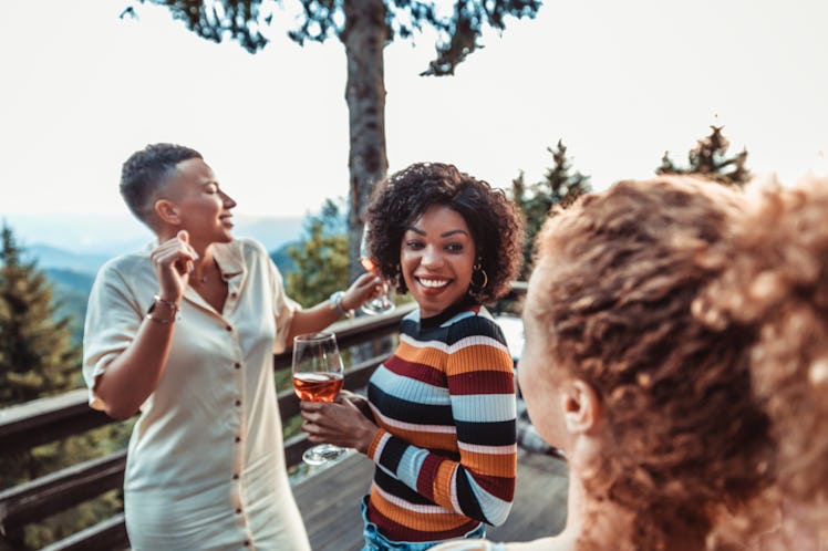 A young Black woman smiles and hangs out with her friends while holding a glass of rosé.