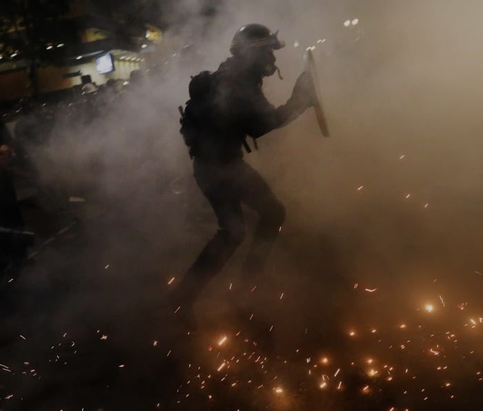 An armed guard can be seen walking through a fog, presumably teargas.
