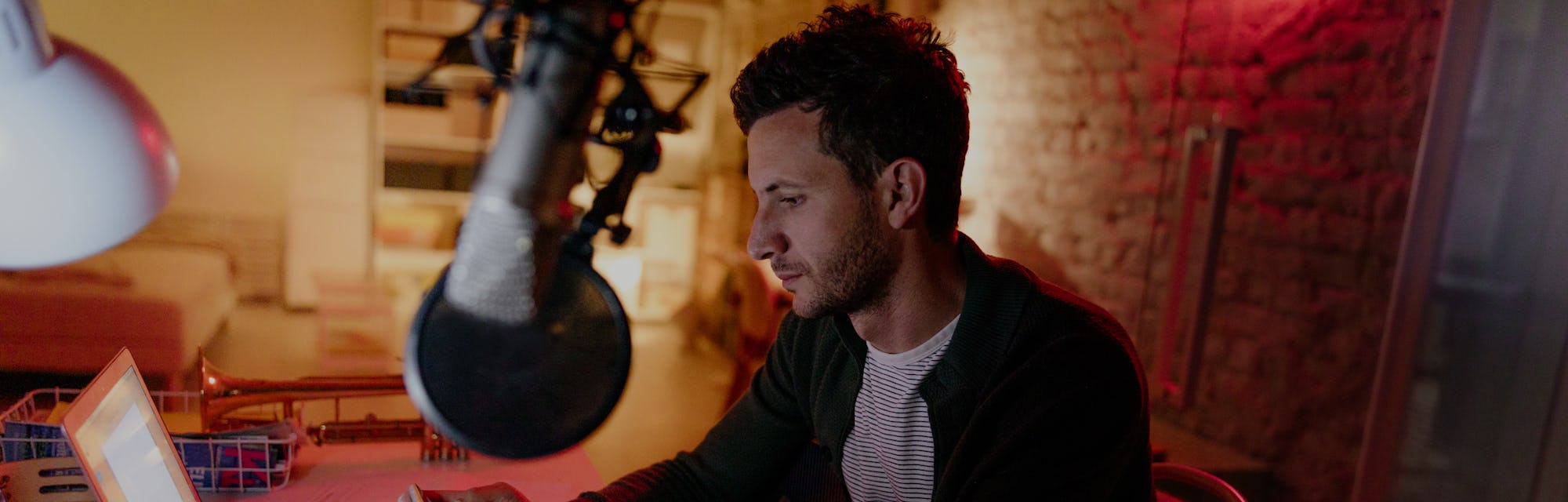 A man can be seen in front of a microphone. He is sitting in front of a desk.