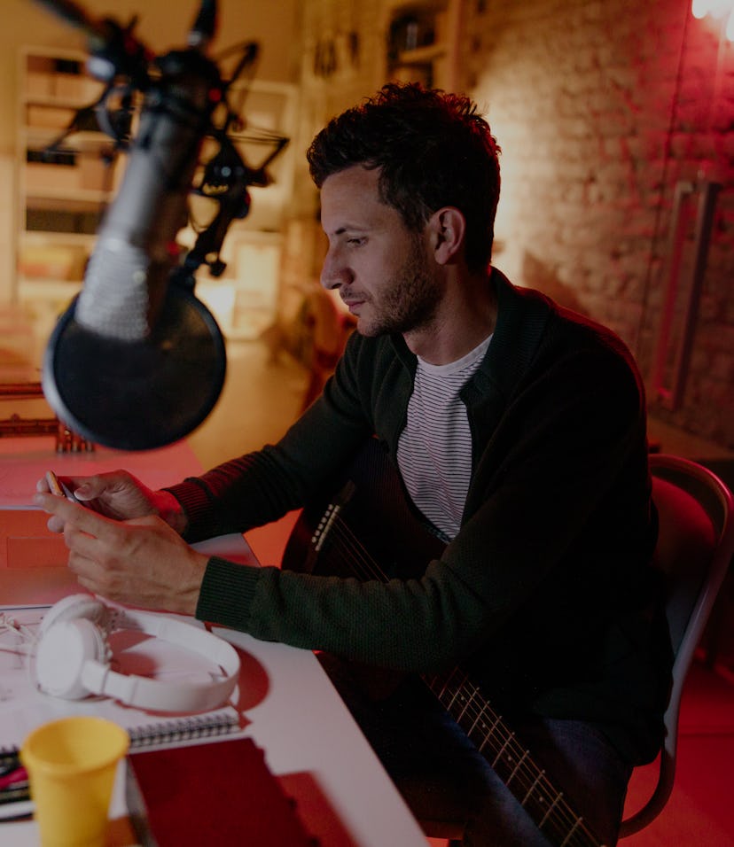 A man can be seen in front of a microphone. He is sitting in front of a desk.