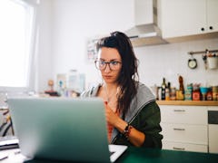 A young woman works at her kitchen table on a summer day with a mug of coffee in her hands.