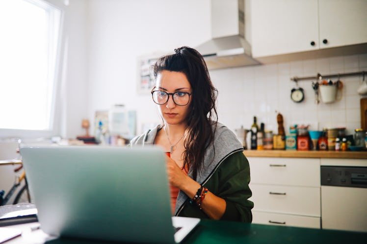A young woman works at her kitchen table on a summer day with a mug of coffee in her hands.