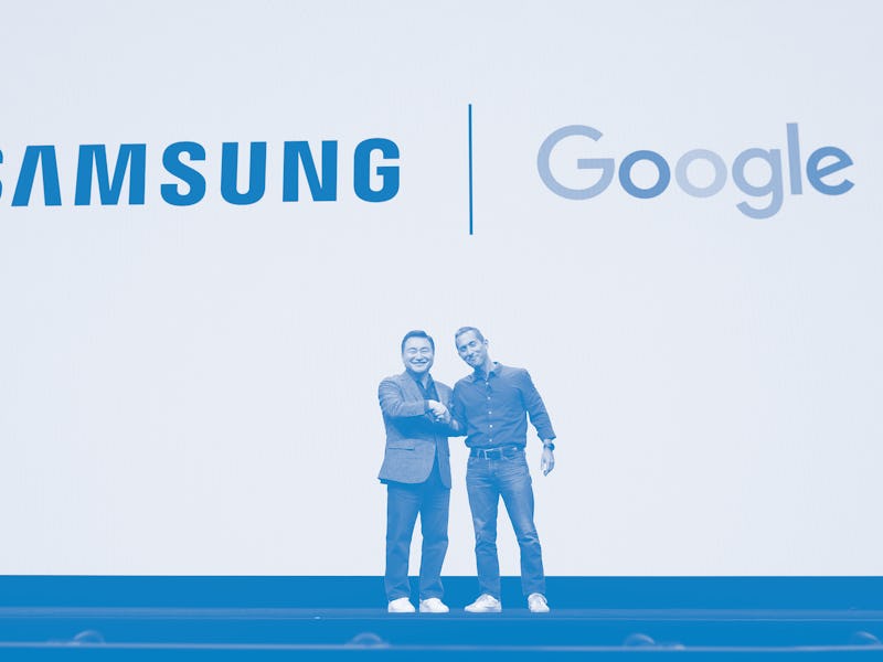 Two men shake hands on stage in front of the Samsung and Google logos.