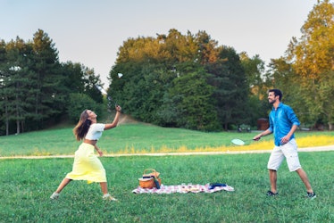 A young couple plays badminton in a grassy field while the sun sets.