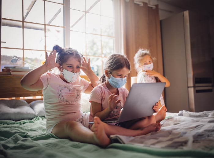 girls sitting on bed wearing face masks looking computer