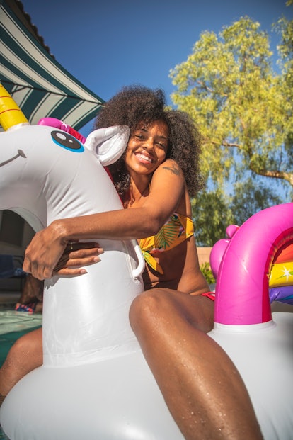 A young Black woman hugs a unicorn pool float while hanging out in the sun on a summer day.