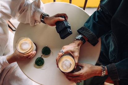 A young couple holds cups of iced coffee and a camera while sitting at a table.