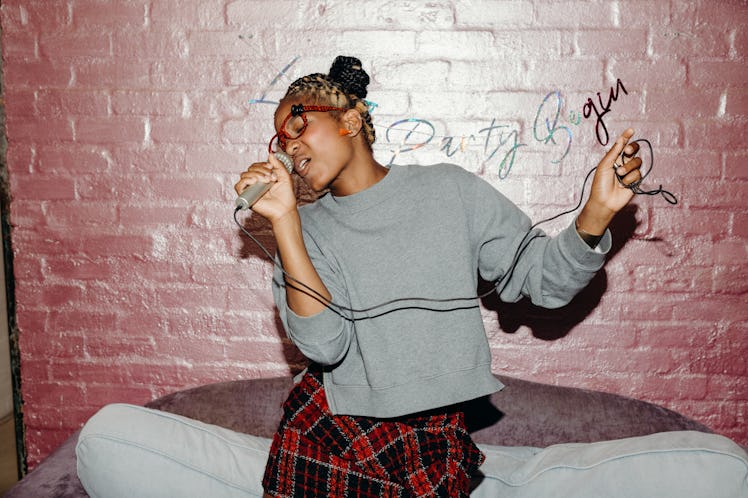 A woman sings karaoke into a microphone, while dancing around her living room.