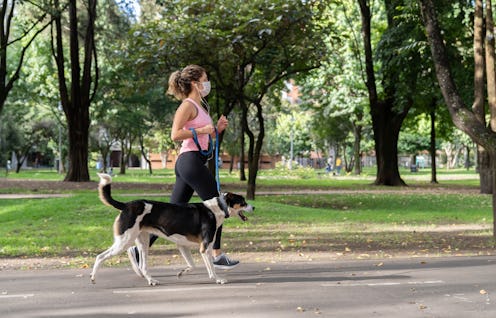 A woman wears a mask while jogging with a dog. Wearing a mask can change the way your body reacts to...