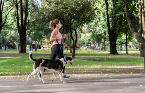 A woman wears a mask while jogging with a dog. Wearing a mask can change the way your body reacts to...