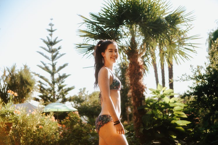 One young woman stands in front of lush trees in a floral bathing suit.