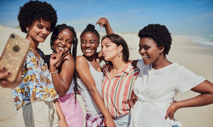A group of friends poses for a selfie on the beach on a sunny day.