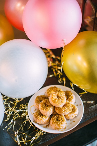 A plate of mini doughnuts sits on a table next to pink and yellow birthday balloons.