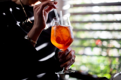 A young woman sips on an Aperol Spritz while sitting near her backyard.