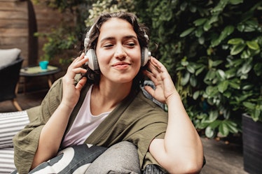 A young woman relaxes in her backyard while wearing a pair of white headphones.