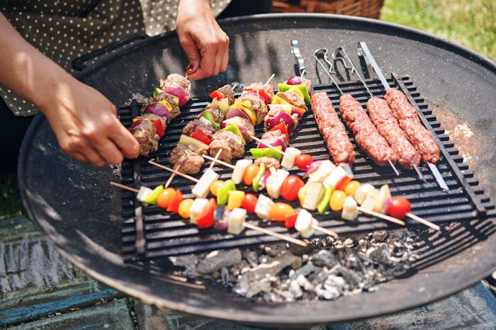 A man grilling vegetable kebabs and shish kebabs on a grill outside during a sunny day