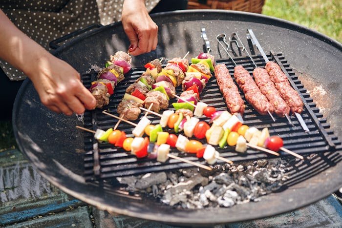 A man grilling vegetable kebabs and shish kebabs on a grill outside during a sunny day