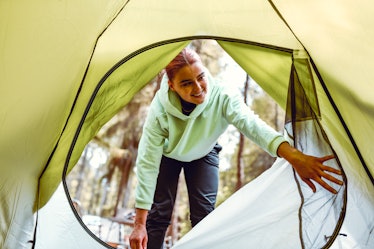 A young woman wearing a green sweatshirt opens up the window of a tent while backyard camping.