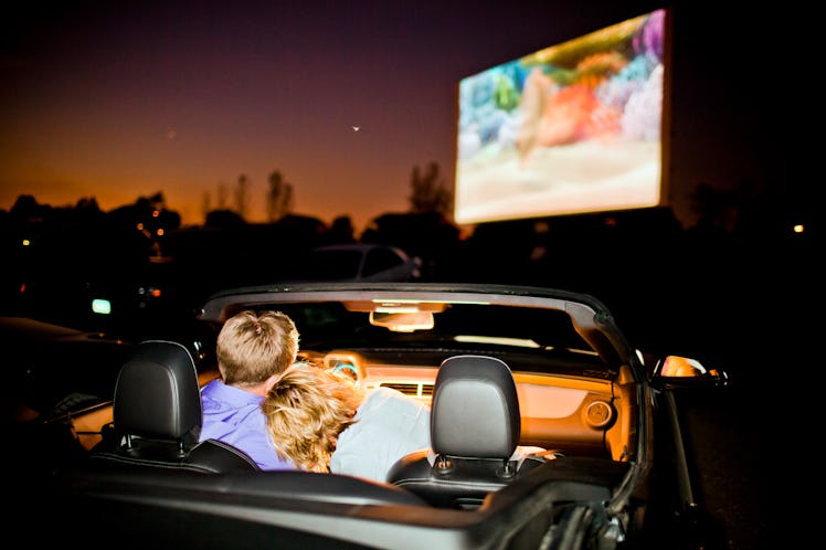 A couple sit in their car at a drive-in movie. 