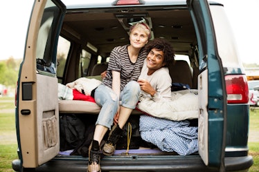 A young woman and her boyfriend sit in the back of campervan while backyard camping.