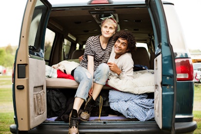 A young woman and her boyfriend sit in the back of campervan while backyard camping.