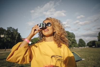 A young Black woman looks up at the sky while holding a disposable camera and backyard camping.