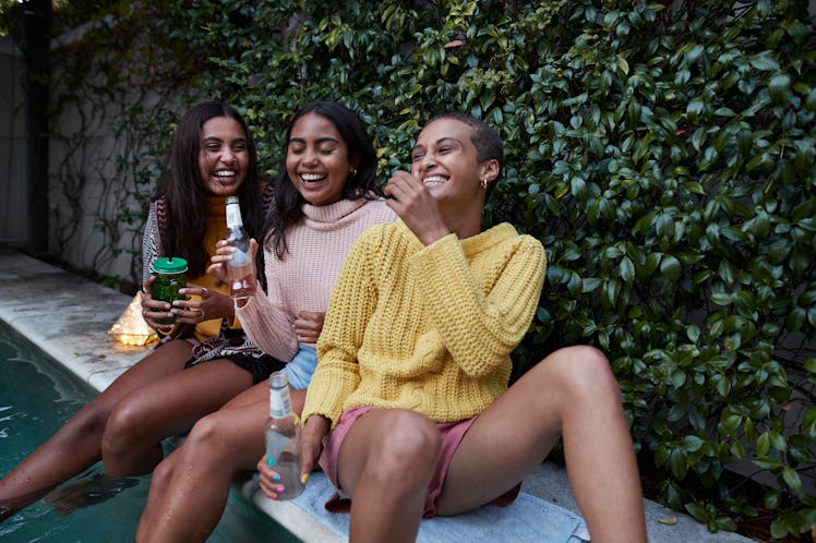 Three roommates sit on the edge of the pool, laughing during the summer.