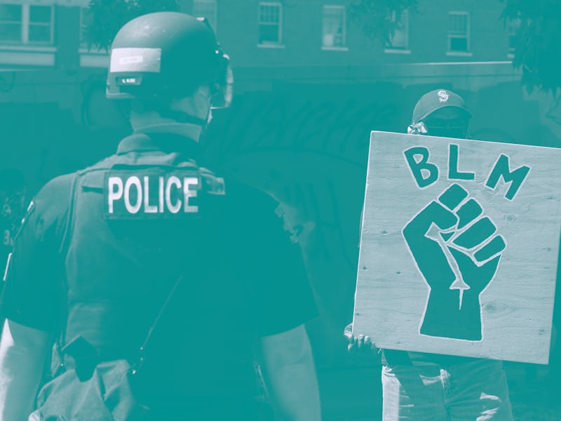 A police officer in uniform faces a protestor with a Black Lives Matter sign.