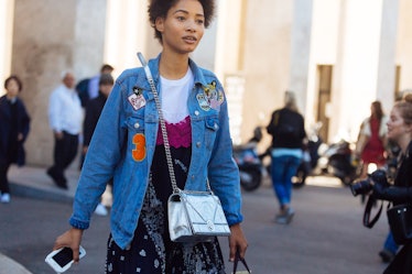 A woman walks through the city with a denim jacket on, covered in patches. 