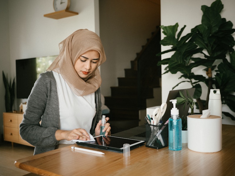 A person wearing a hijab cleans and organizes her desk space at home. Employing multiple different t...